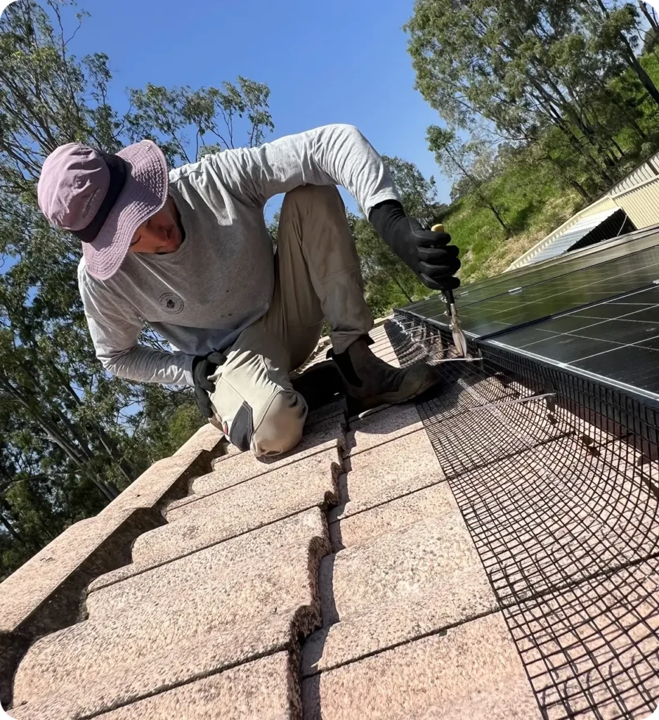 Technician installing bird proofing mesh around rooftop solar panels on a tiled roof