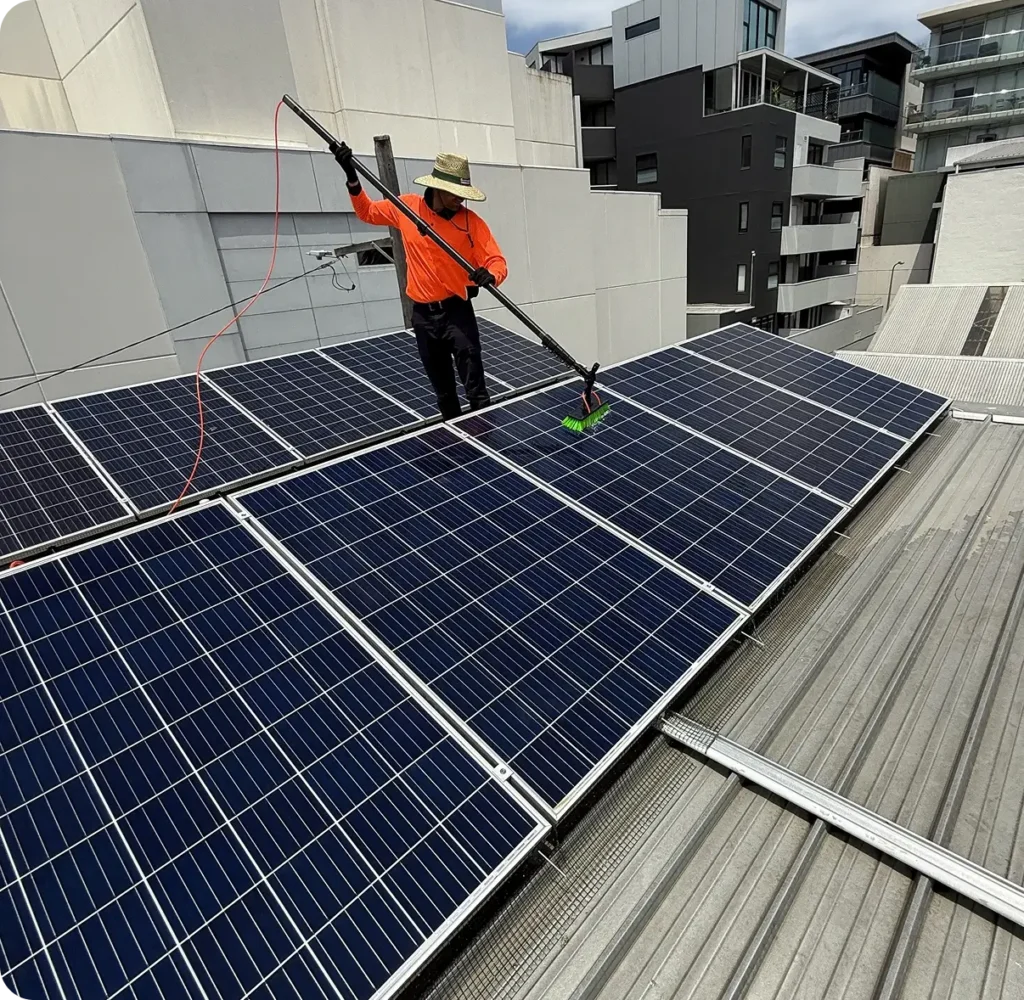 Technician cleaning rooftop solar panels using a soft brush and purified water system